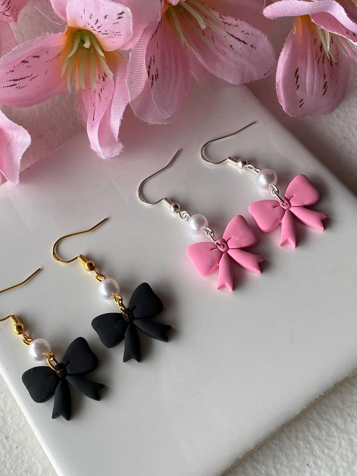 three pairs of pink and black bow earrings on a white surface with flowers in the background