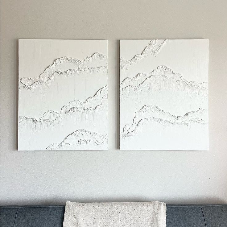 two white paintings are hanging on the wall above a couch with a blanket draped over it