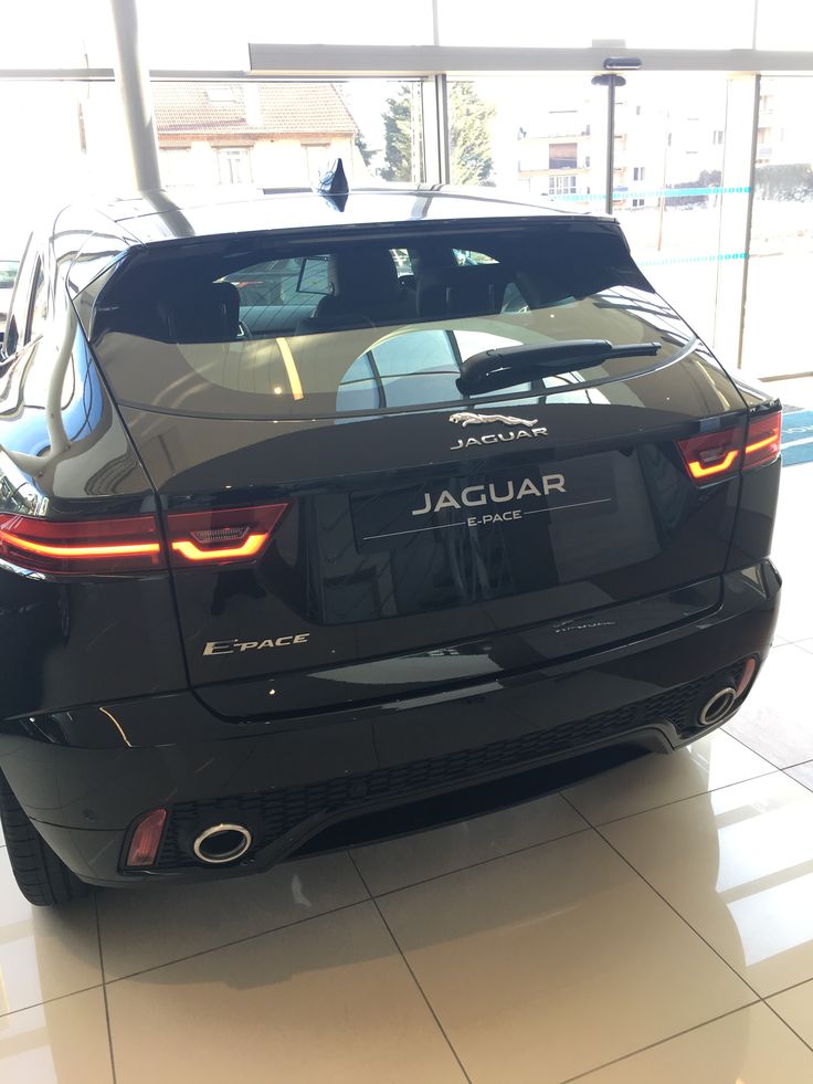 the back end of a black jaguar car in a showroom with its lights on