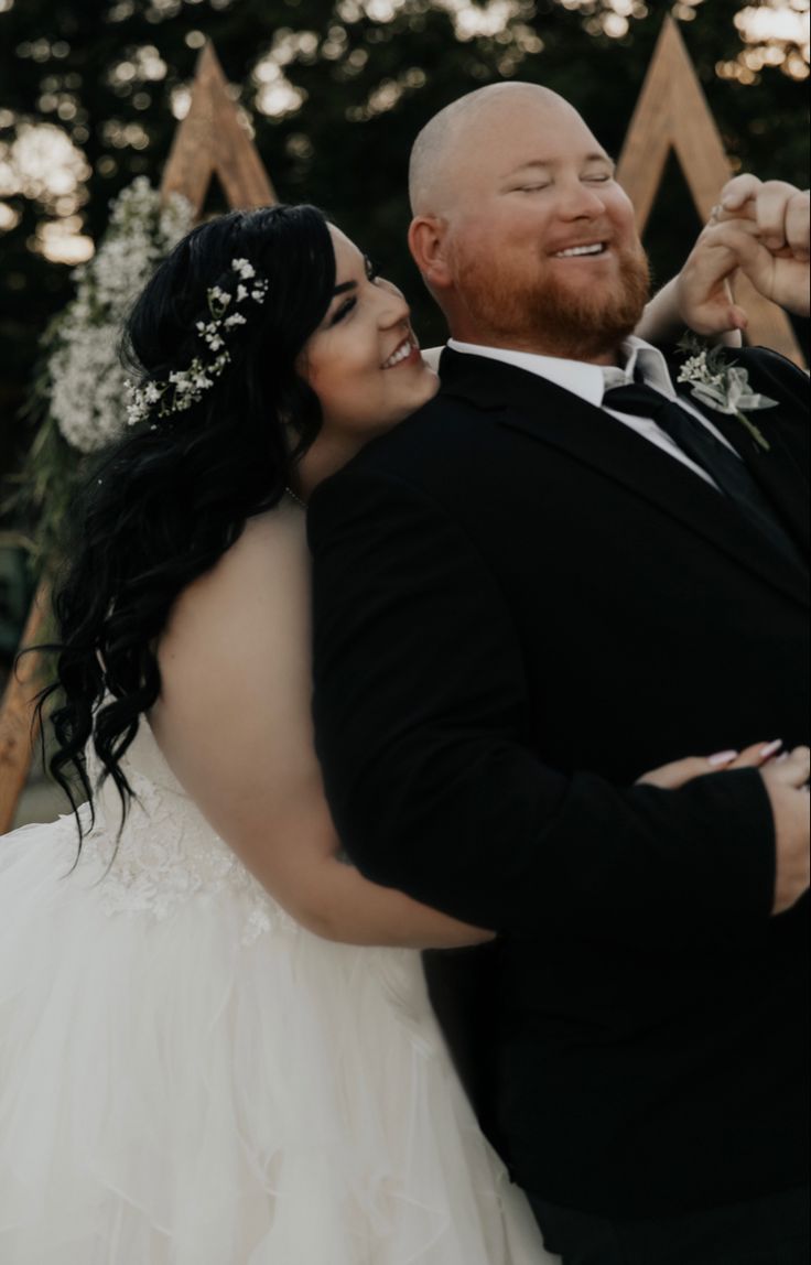 a bride and groom pose for a wedding photo in front of an outdoor ceremony arch