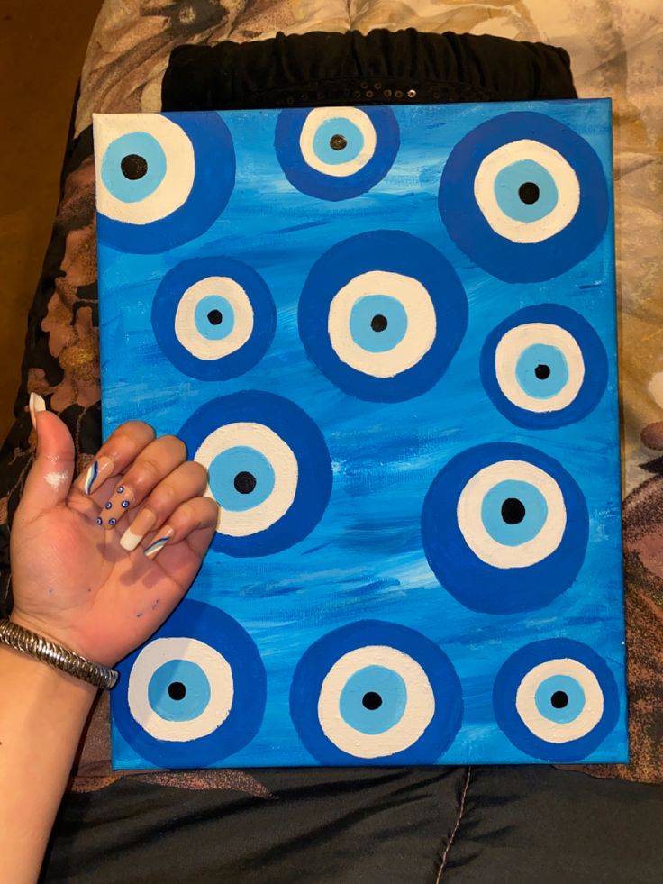 a woman is holding up a painting with blue and white circles painted on the canvas