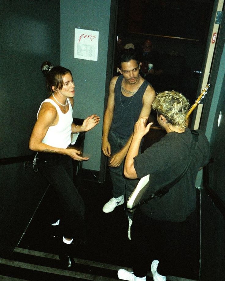 two people standing in front of a door talking to each other while another person holds up a bat