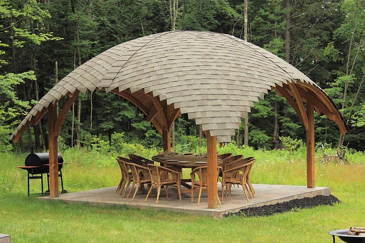 a large wooden gazebo sitting on top of a lush green field next to a forest