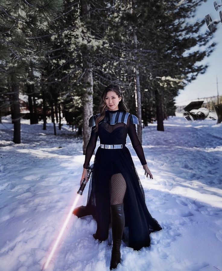 a woman in a star wars outfit standing in the snow with lightsabed behind her