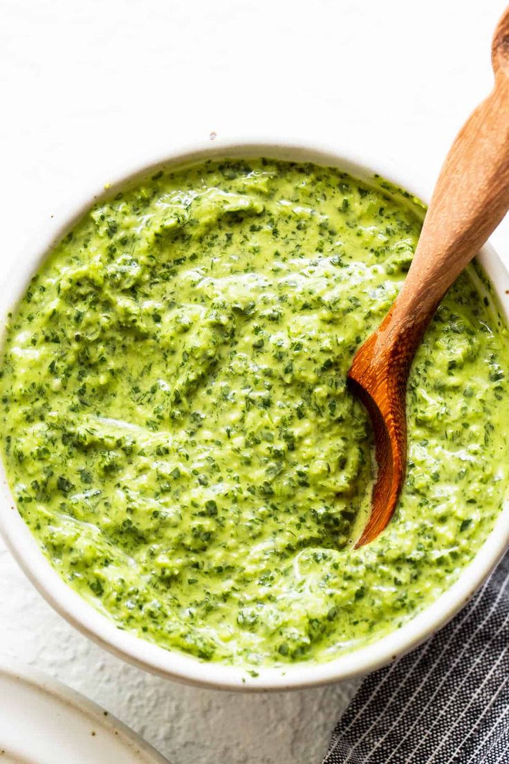 a wooden spoon in a white bowl filled with pesto