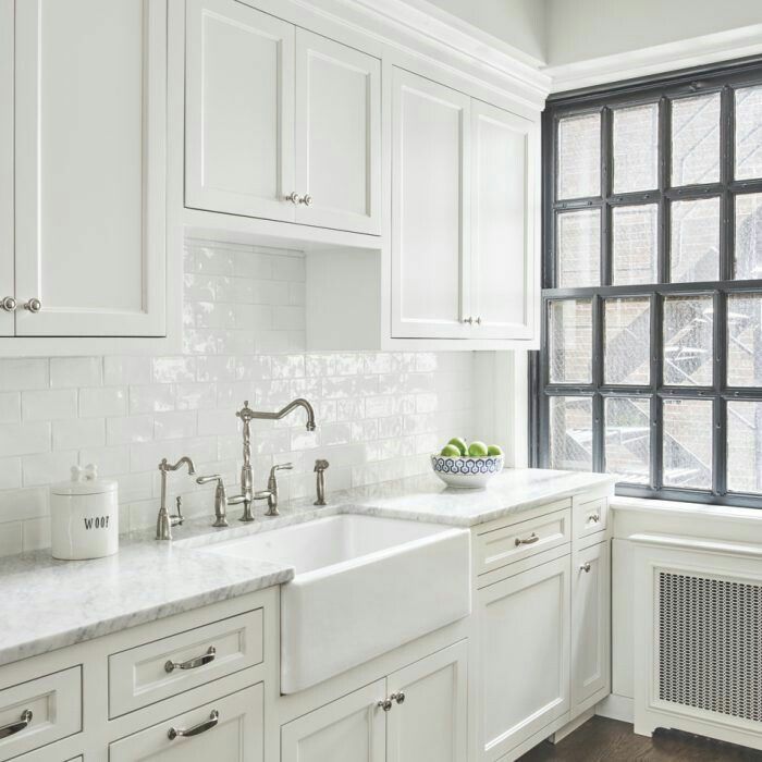 a kitchen with white cabinets and marble counter tops, along with a window that looks out onto the street