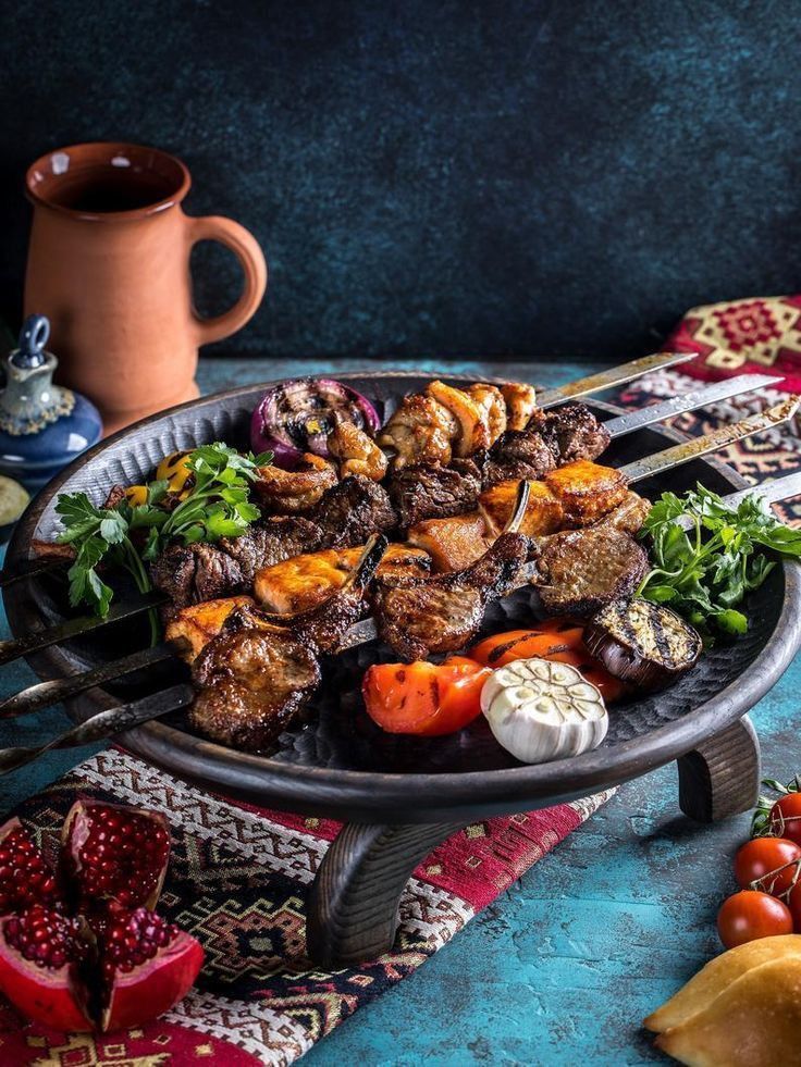 a platter filled with meat and vegetables on top of a blue table cloth next to a mug