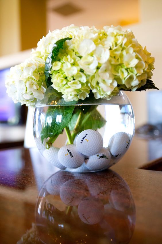 a vase filled with white flowers and golf balls on top of a wooden table next to a tv