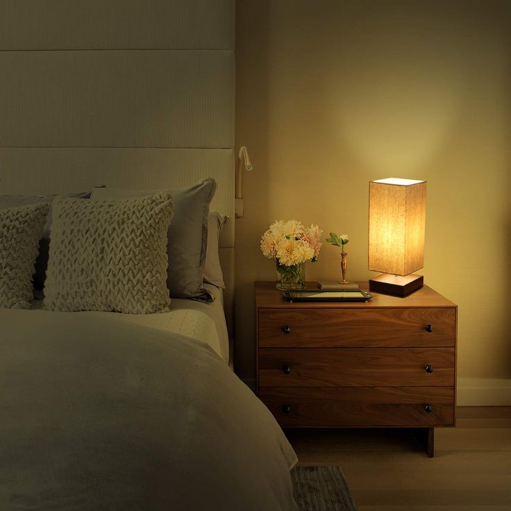 a bedroom with a bed, night stand and lamp on the bedside table next to it