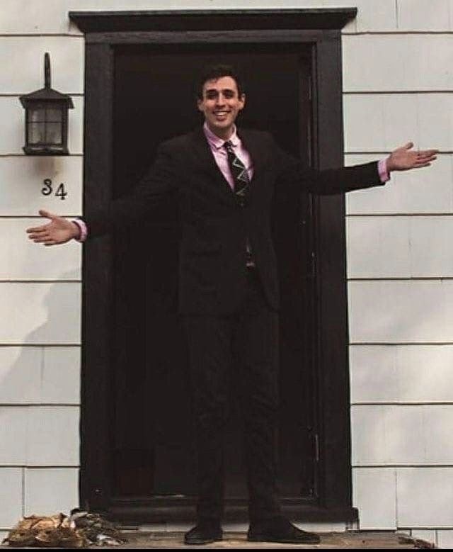 a man in a suit and tie standing on the front steps of a house with his arms outstretched