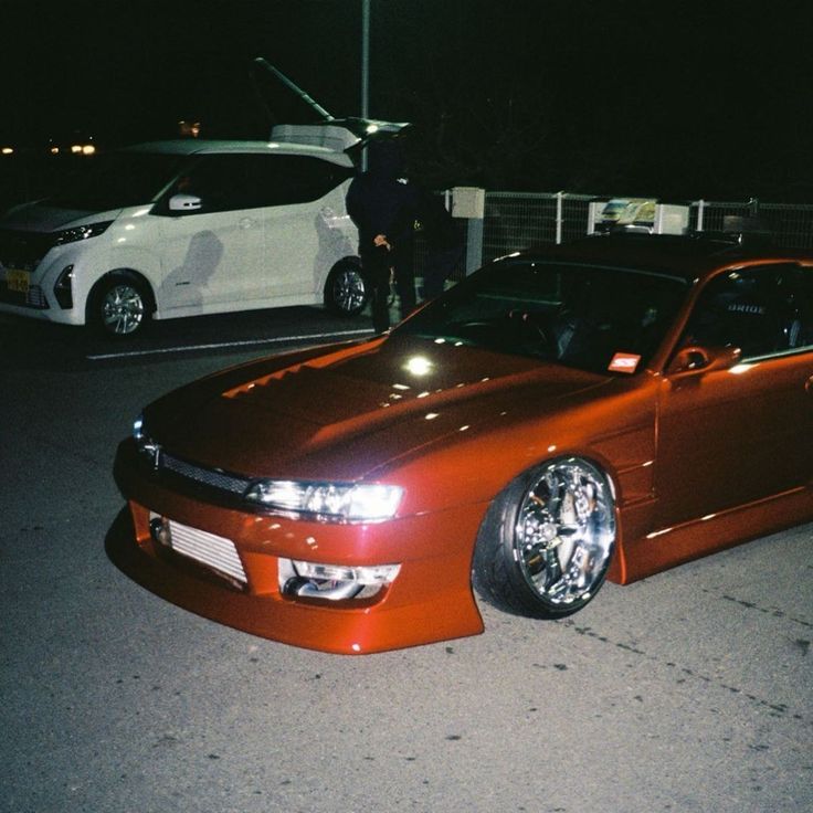 a red car parked next to a white car in a parking lot at night time