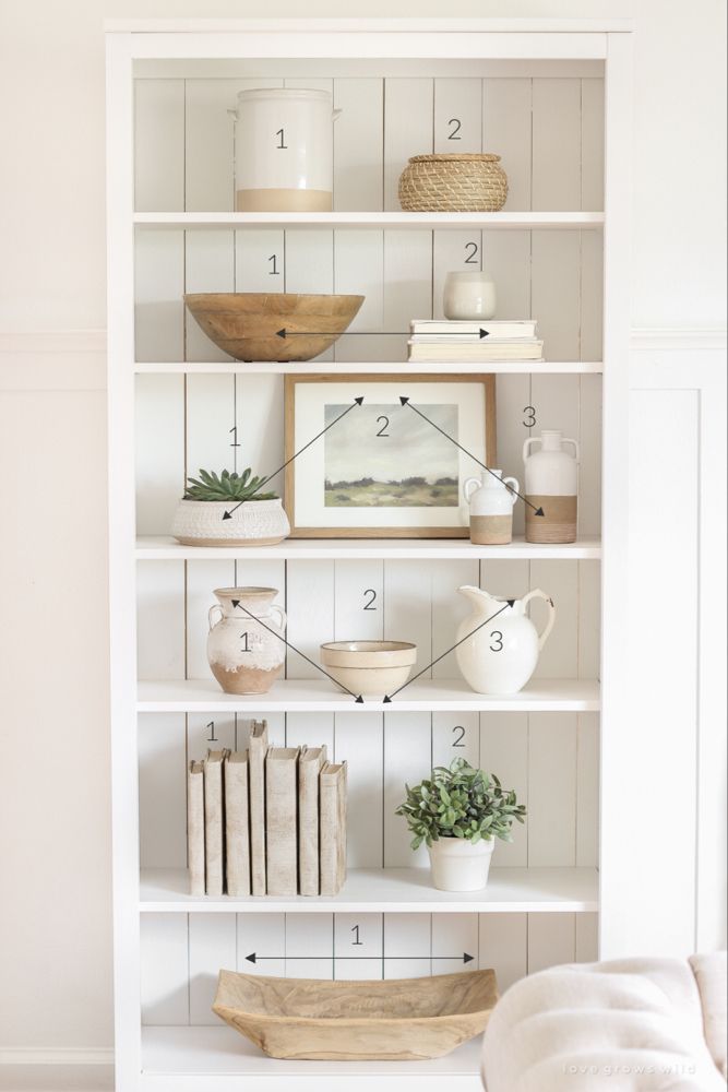 a white bookcase filled with lots of books next to a wall mounted clock and vases