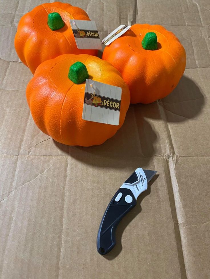 four orange pumpkins sitting on top of a cardboard box next to a pair of scissors