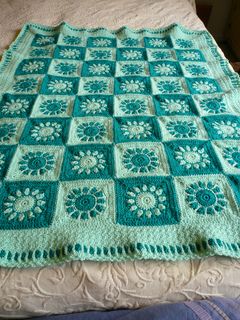 a green crocheted blanket on top of a bed with white and blue flowers