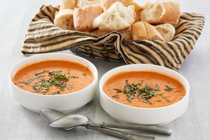 two bowls of tomato soup with bread on the side