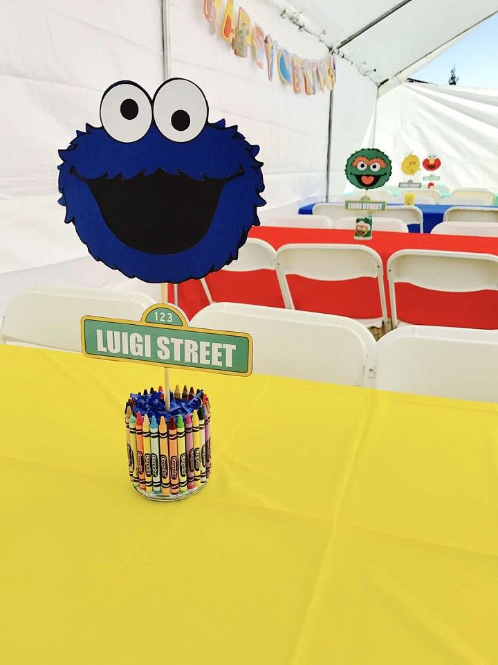 a sesame street sign and some crayons in front of a table with chairs