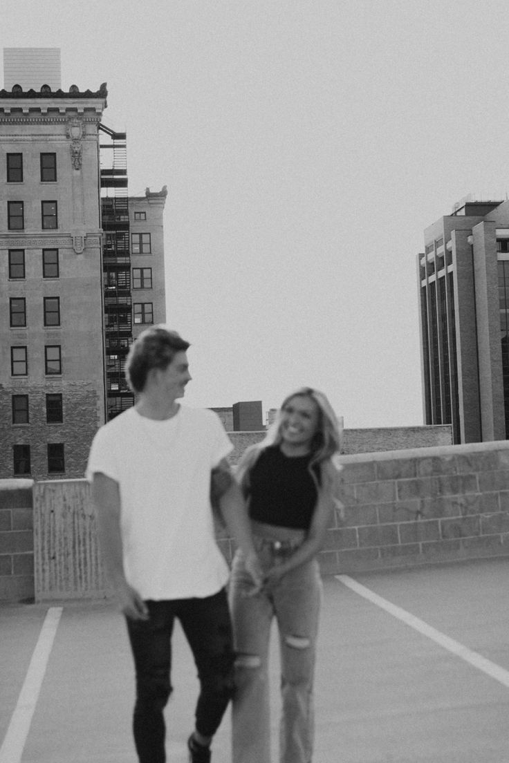 a man standing next to a woman on top of a skateboard in a parking lot