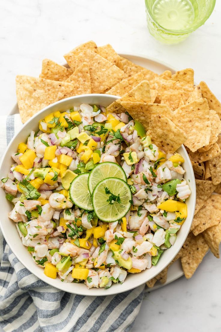 a white bowl filled with guacamole, corn and salsa surrounded by tortilla chips