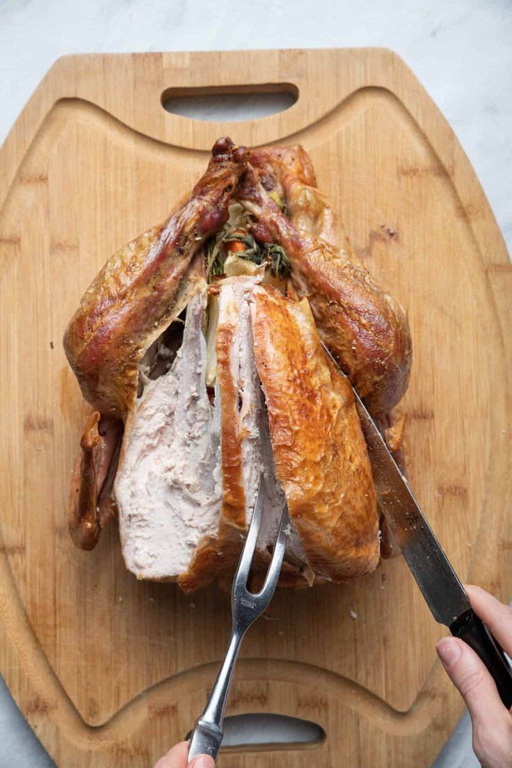 a person cutting up a turkey on top of a wooden cutting board with a knife