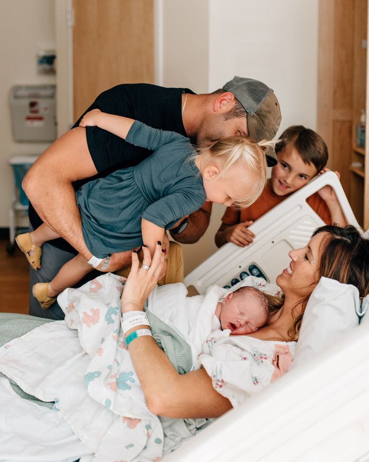 a man and two women are looking at a baby in a crib while three other people look on