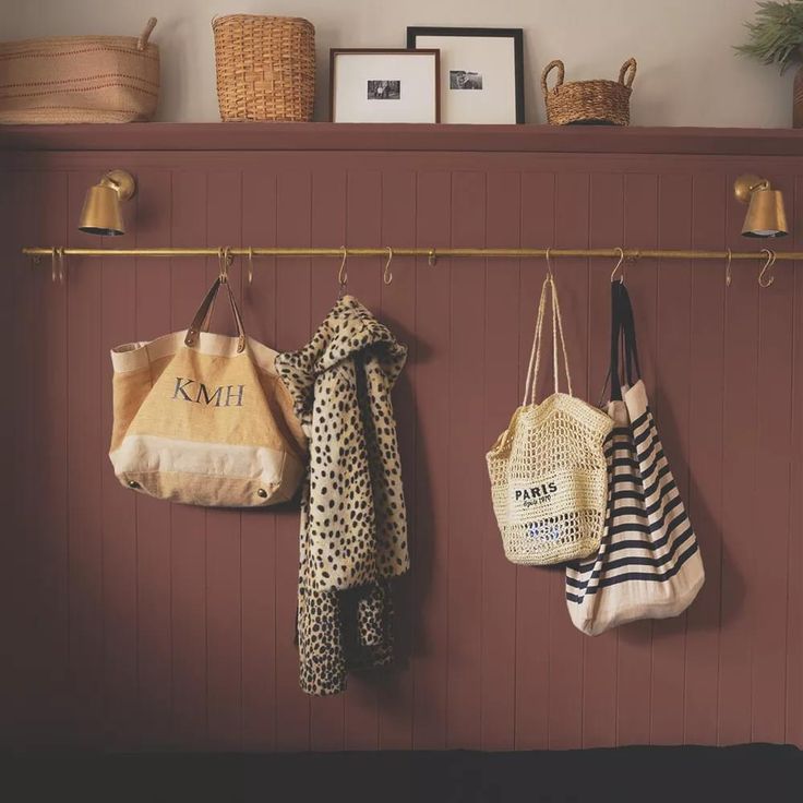 three purses hanging from hooks on a red wall next to baskets and other items