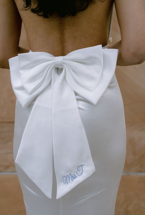 the back of a woman wearing a white dress with a large bow on her waist