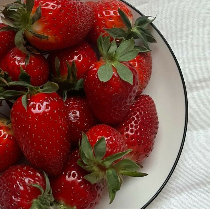 a white plate topped with lots of ripe strawberries on top of a table cloth