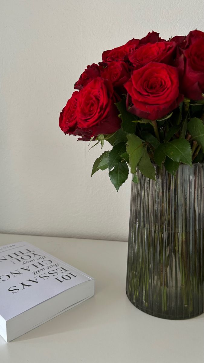 a bouquet of red roses in a vase next to a book on a white table