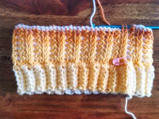 an orange and white knitted object on a wooden table next to a knitting needle