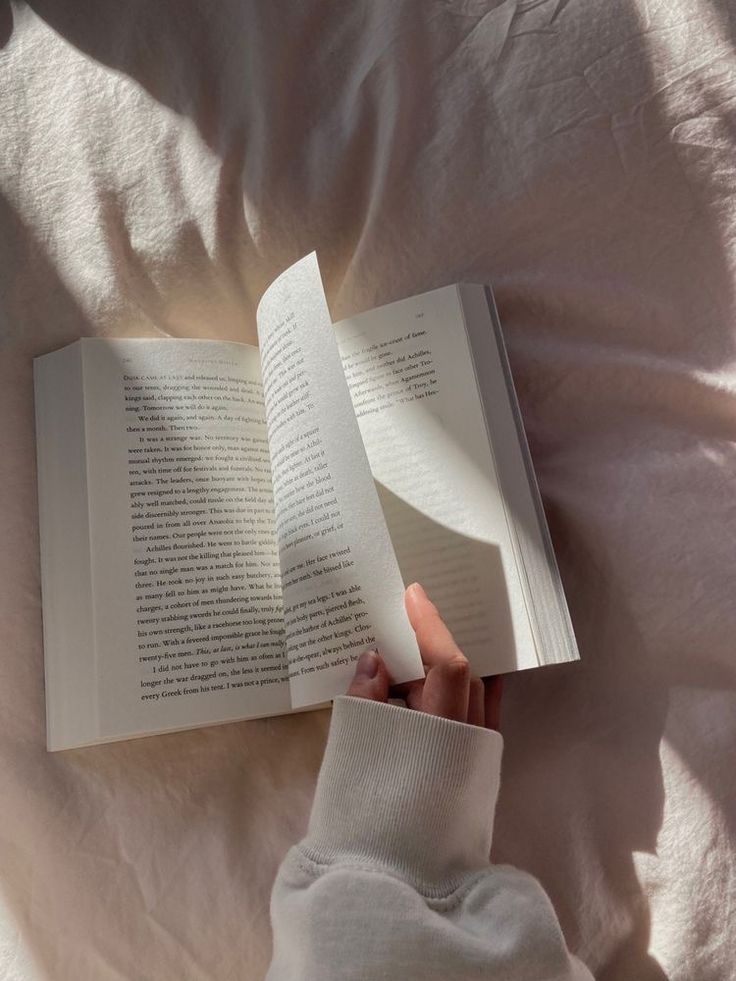 someone is reading a book in bed with their hand on top of the open book