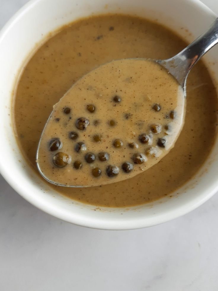 a white bowl filled with soup on top of a marble counter next to a spoon