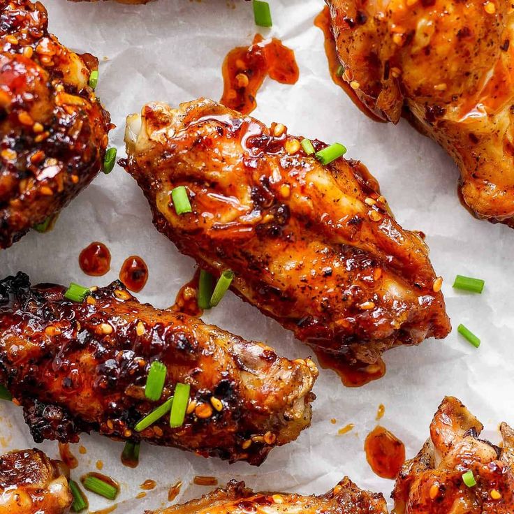 chicken wings with sauce and scallions on top of parchment paper, ready to be eaten