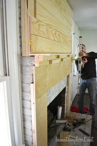 a man standing next to a fire place in a living room under construction with wood planks on the wall