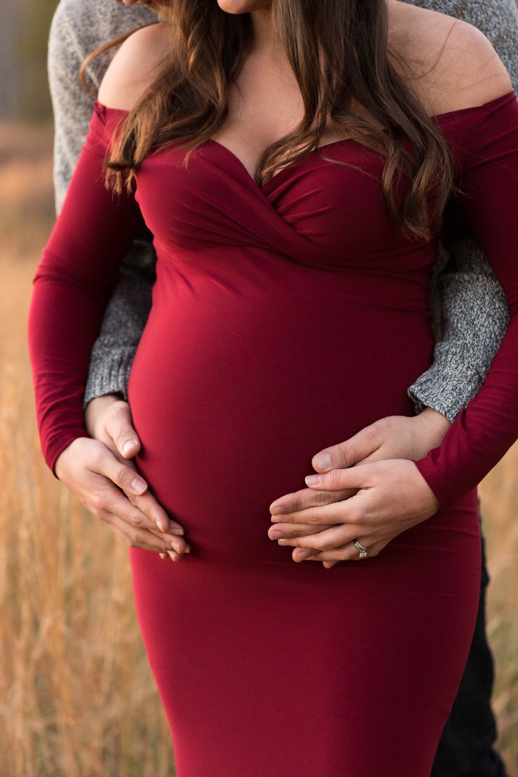 a pregnant woman in a red dress is holding her husband's belly