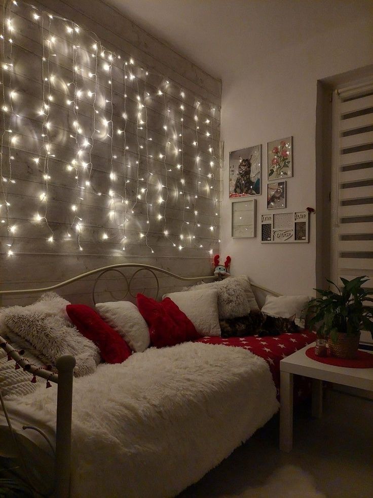 a white bed with red pillows and lights on the wall behind it in a bedroom