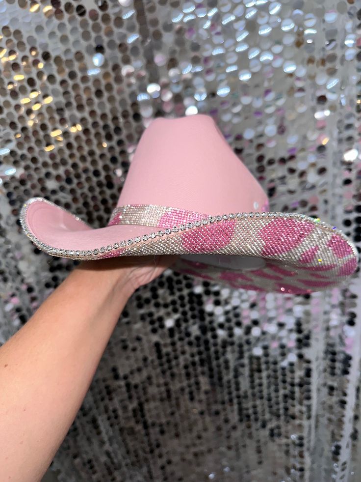 a pink cowboy hat with sequins is held up by a woman's hand