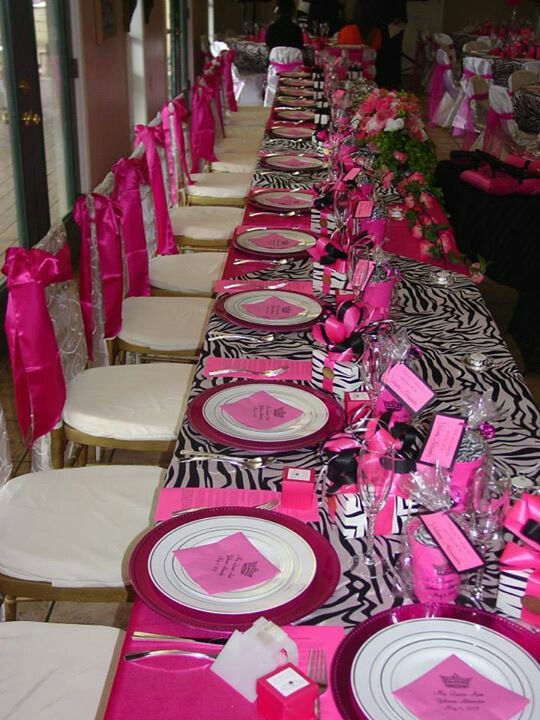 a long table set with pink and white plates, napkins and place settings for an event