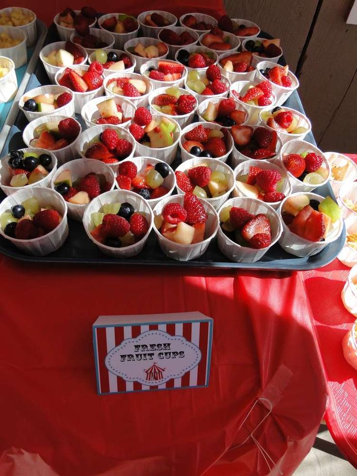 a table topped with lots of cups filled with fruit and muffins on top of red cloth covered tables