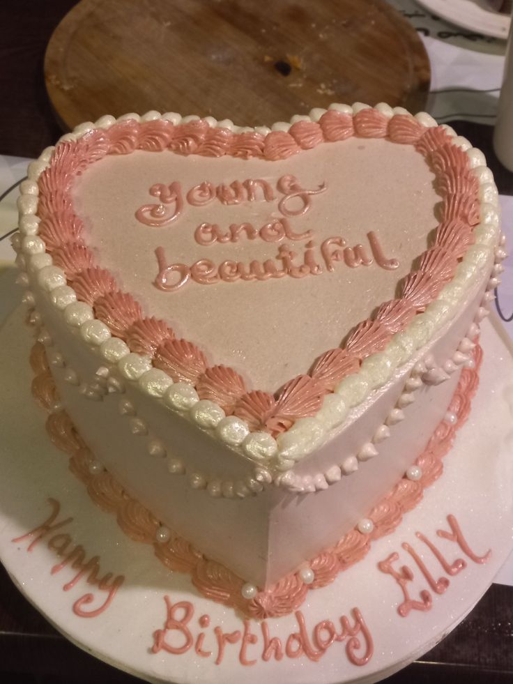 a heart shaped birthday cake with writing on the top and bottom, sitting on a table