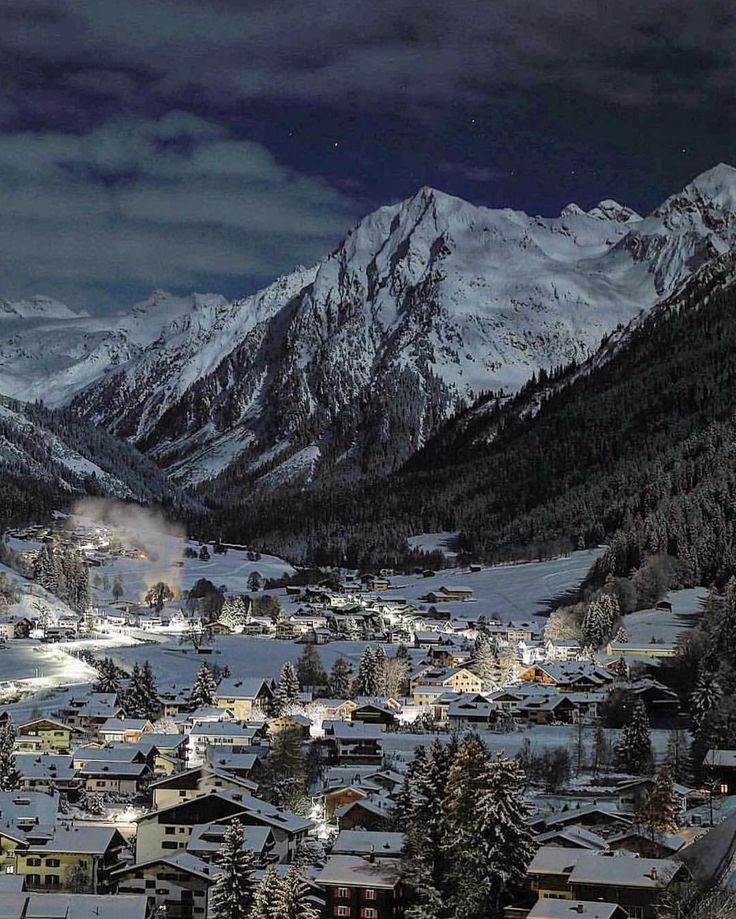 a snowy mountain town with snow covered mountains in the background and dark clouds above it