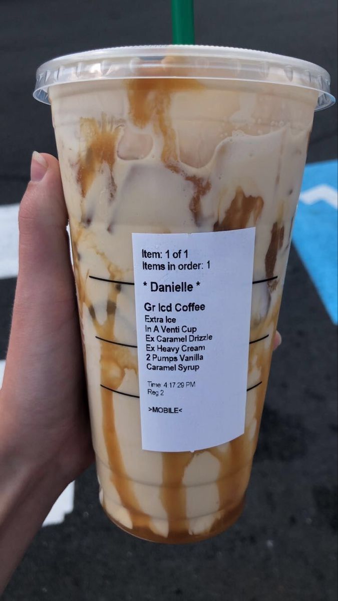 a person holding up a cup with ice cream and caramel on it in front of a parking lot