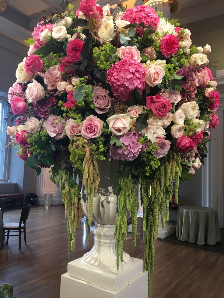 a large arrangement of flowers on display in a room with wooden flooring and white pedestals