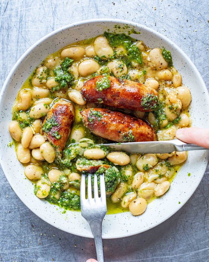 someone is holding a fork over a bowl of chicken and beans with pesto sauce