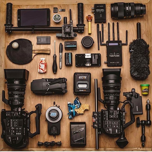 a wooden table topped with lots of different types of cameras and equipment on top of it