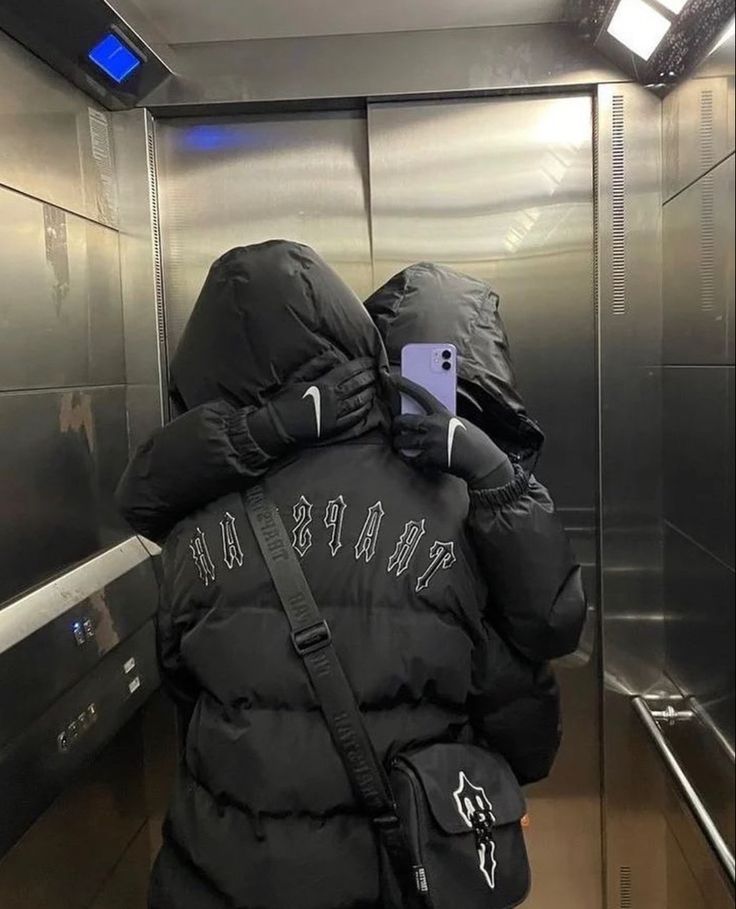 a person in a black jacket is standing on an elevator and looking at their cell phone