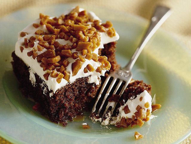 a piece of cake with white frosting and nuts on top is being held by a fork