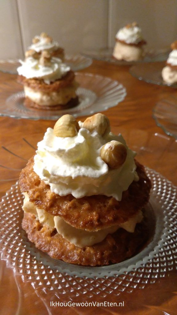 some desserts are sitting on glass plates on a wooden table and one is topped with whipped cream