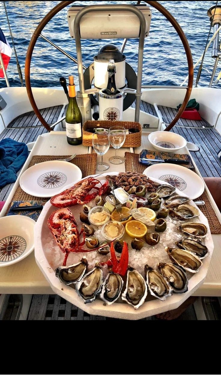 a large platter of oysters and wine on a sailboat in the ocean