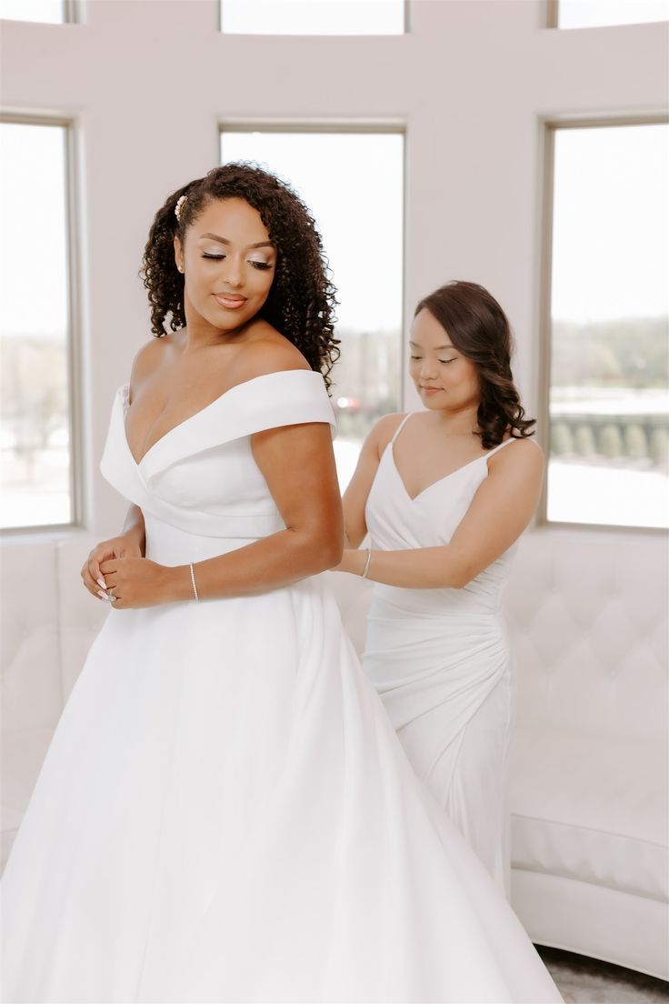 two women in white dresses standing next to each other and one is wearing a wedding dress