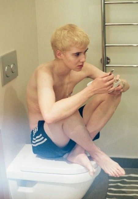 a young man sitting on top of a toilet in a bathroom next to a towel rack